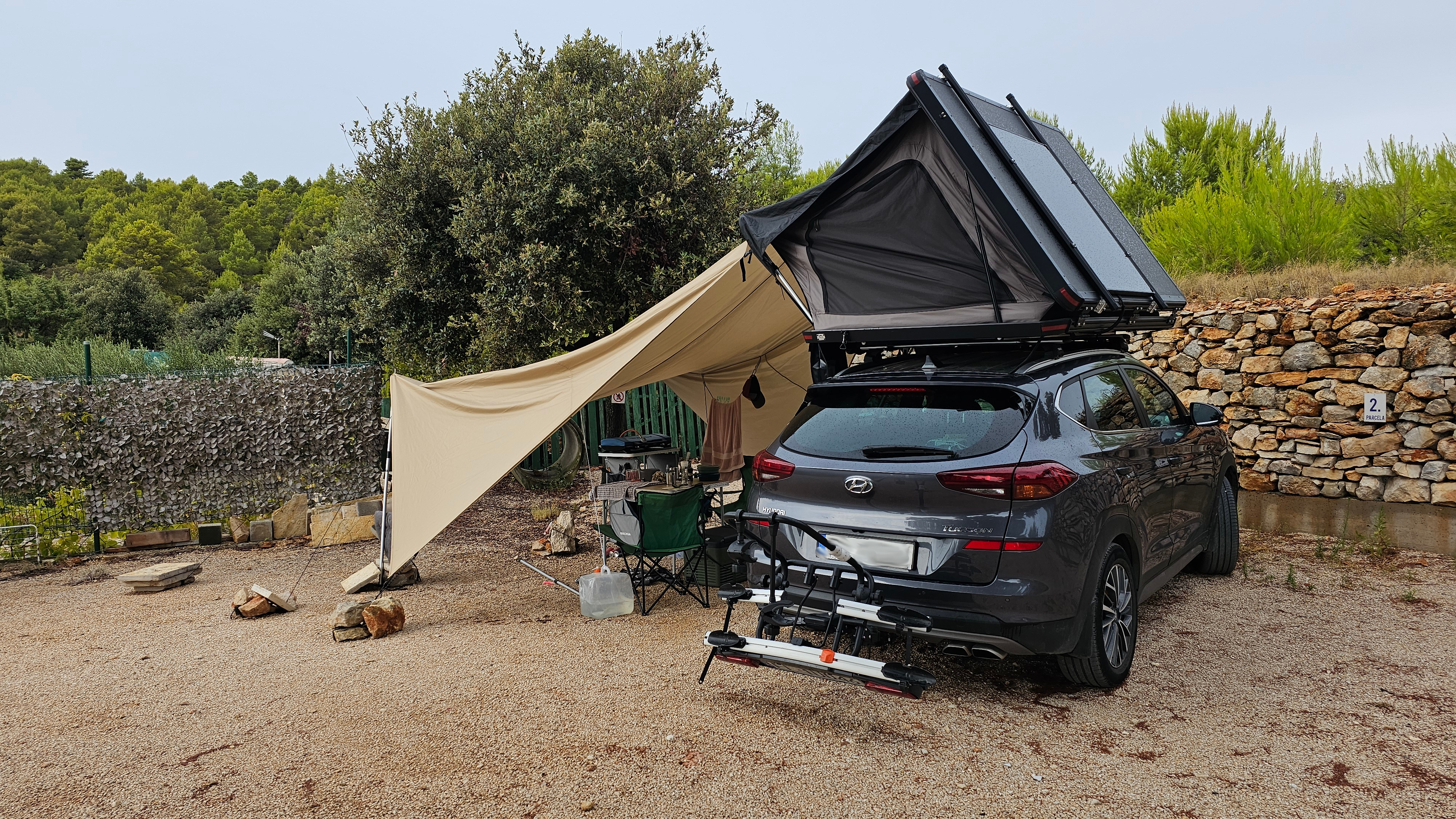 Campsite with the rooftop tent and awning deployed against a forest backdrop.