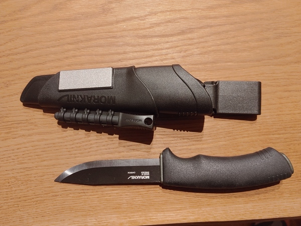 A Morakniv survival knife with a carbon steel blade in its sheath.